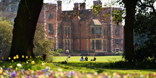 Heslington Hall with tress and people walking on the grass in front of the building.